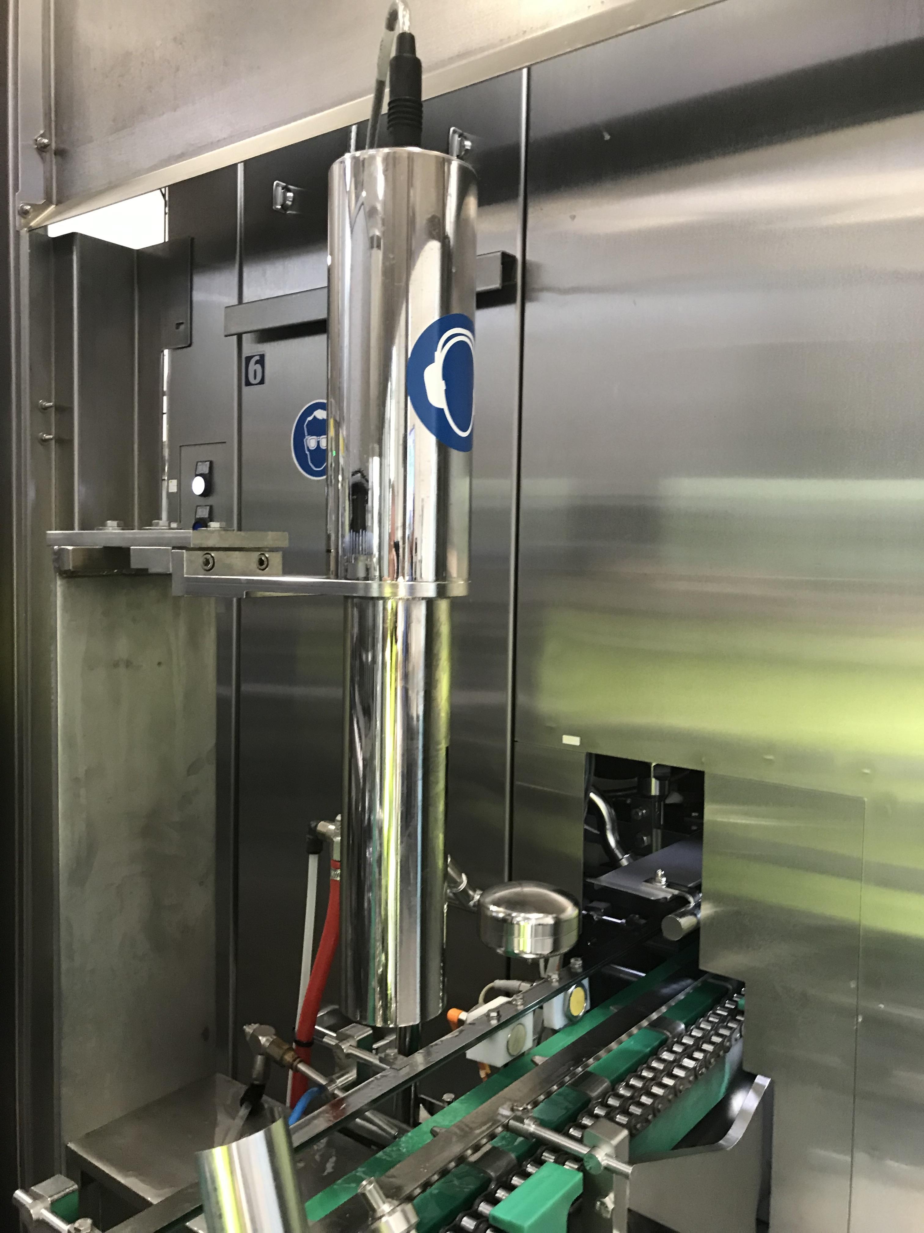 Stainless steel S-300 transducer mounted above a green conveyor system inside an industrial packaging machine.